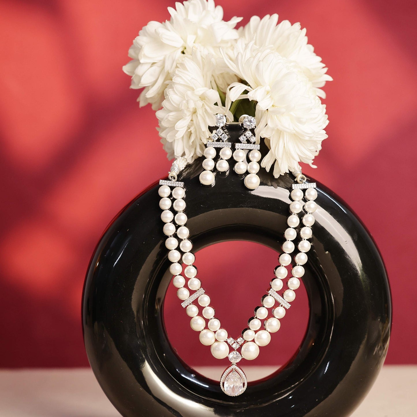 Pearl necklace and earrings on a black plate with white flowers against a red background
