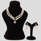 Pearl necklace and earrings set on a black mannequin and stand against a gray background